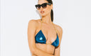 Woman in metallic blue bikini top with gold straps and black sunglasses against white background