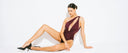Woman in a maroon cut-out one-piece bodysuit posing against a white background