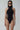 Woman wearing black sustainable bodysuit with mesh side panels and high neckline, fashion pose