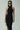 Woman in black halter neck dress with sunglasses, cream handbag, and silver bangles