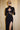 Woman in a black cut-out evening dress with sheer panels, high slit, gloves, and sunglasses