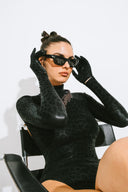 Side view of the Room 24 Jane black bodysuit showing its open-back design, fitted sleeves and tonal leopard finish.