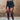 Woman in black long-sleeve bodysuit with cut-outs and sheer tights standing indoors