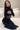 Woman in black cut-out mesh dress with long sleeves sitting on a white bed