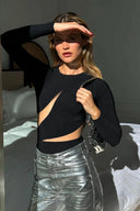 Woman wearing black cut-out bodysuit and metallic silver skirt, posing in sunlight.